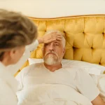 Personne au lit avec des mouchoirs et un verre d'eau, montrant les soins à domicile pour la grippe