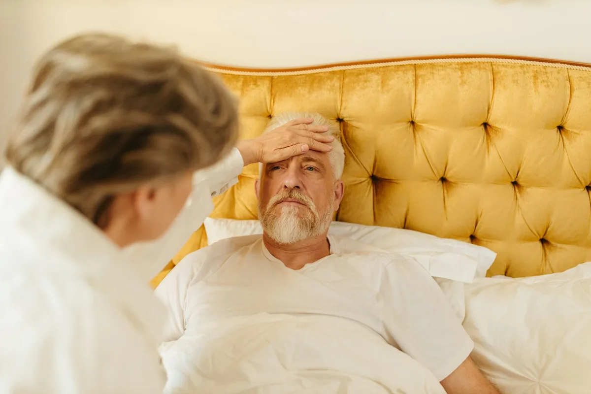 Personne au lit avec des mouchoirs et un verre d'eau, montrant les soins à domicile pour la grippe