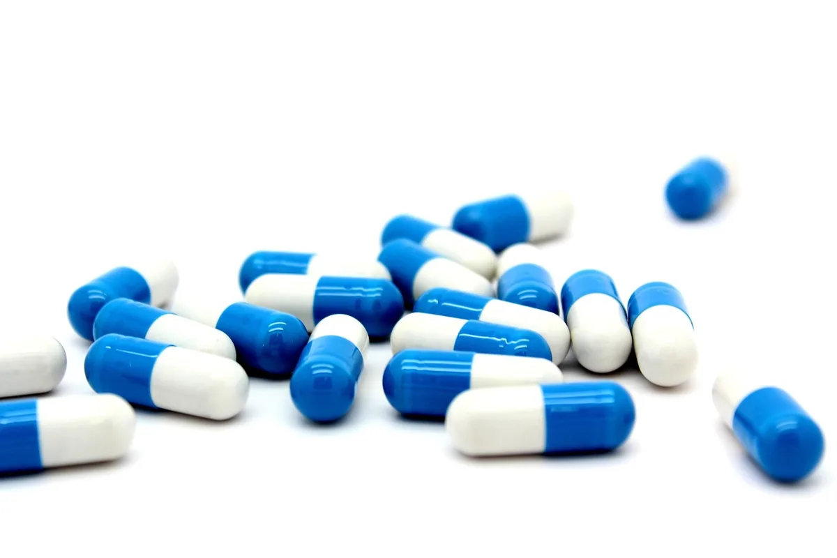 Mains tenant une capsule et un flacon de médicament avec un verre d'eau, illustrant les interactions entre suppléments e