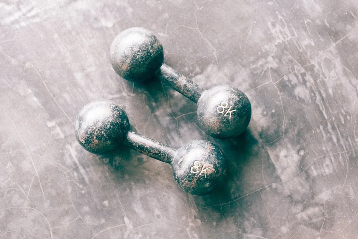 Personne anonyme faisant des exercices de musculation avec haltères près d'une fenêtre en journée