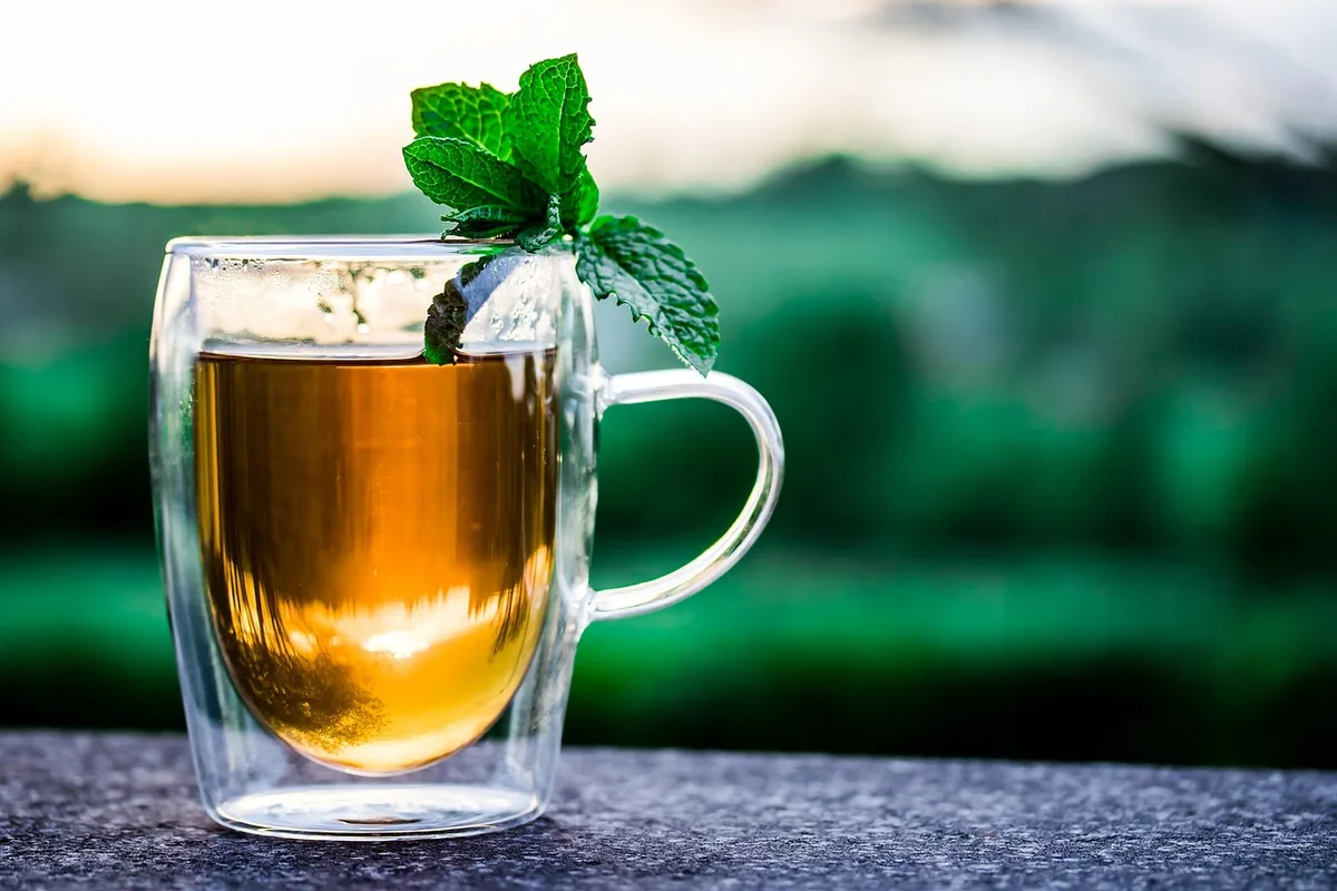 Tasse de thé vert avec feuilles sèches à côté dans une cuisine lumineuse