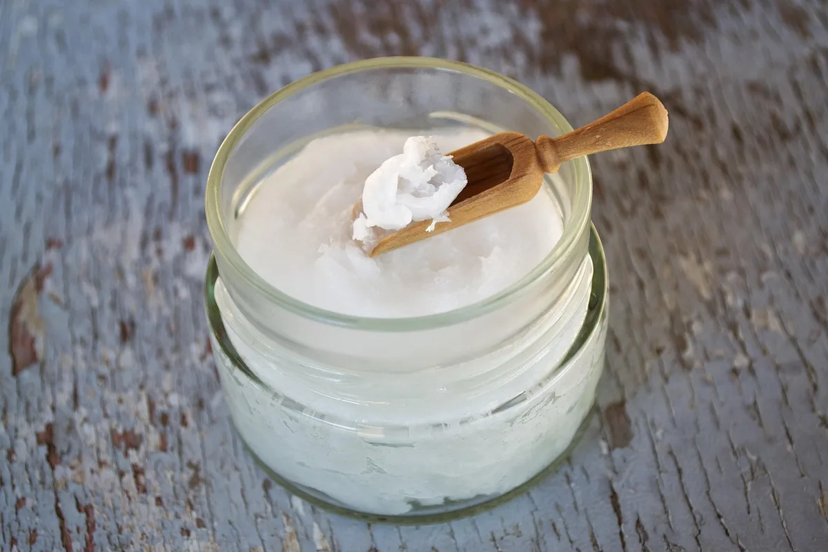 Application d'une petite quantité d'huile de coco sur les longueurs des cheveux près d'une fenêtre